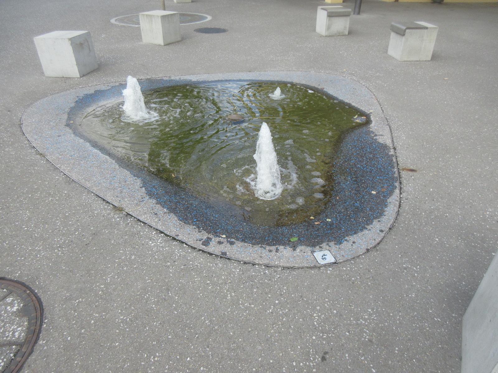 Zentrum Rössli *** 2018 (Neugestaltung des Platzes gem. Luftbild) *** Asphalt mit blauen Steinchen *** -- *** Springbrunnen; kein Trinkwasser