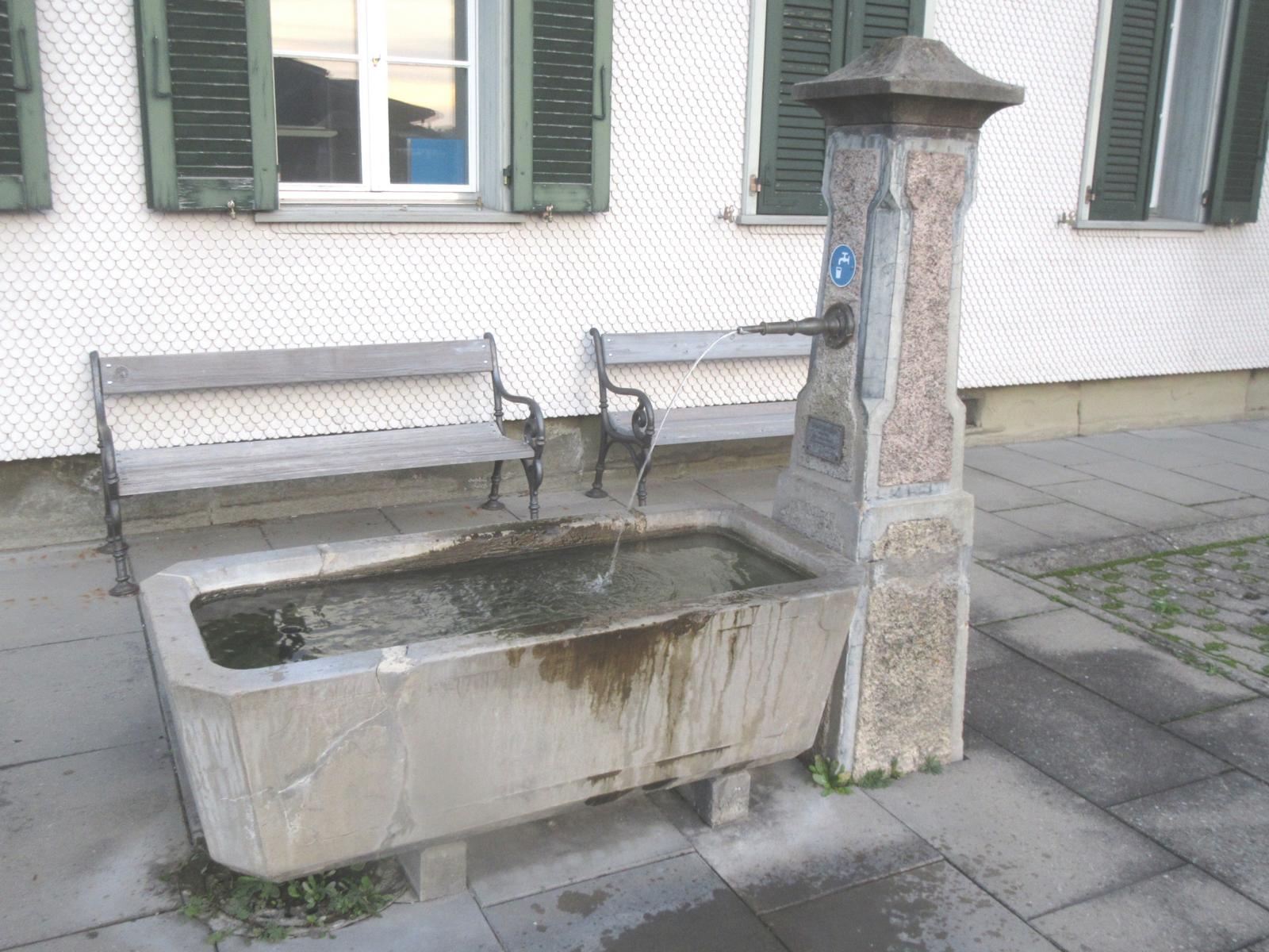 Gemeindehaus *** o.J. (20. Jh.) *** Beton; schmuckloser Trog *** Beton; Messingrohr; Stock mit Schmuckfeldern, Aufsatz: Pyramidenstumpf *** Tafel: "Trinkwasser von der Vennersmühle Wasserversorgung" (heute: Emmental Trinkwasser) , <a href="./files/wasseranalyse_be_-_aefligen.pdf" target="_self">Wasseranalyse</a>
